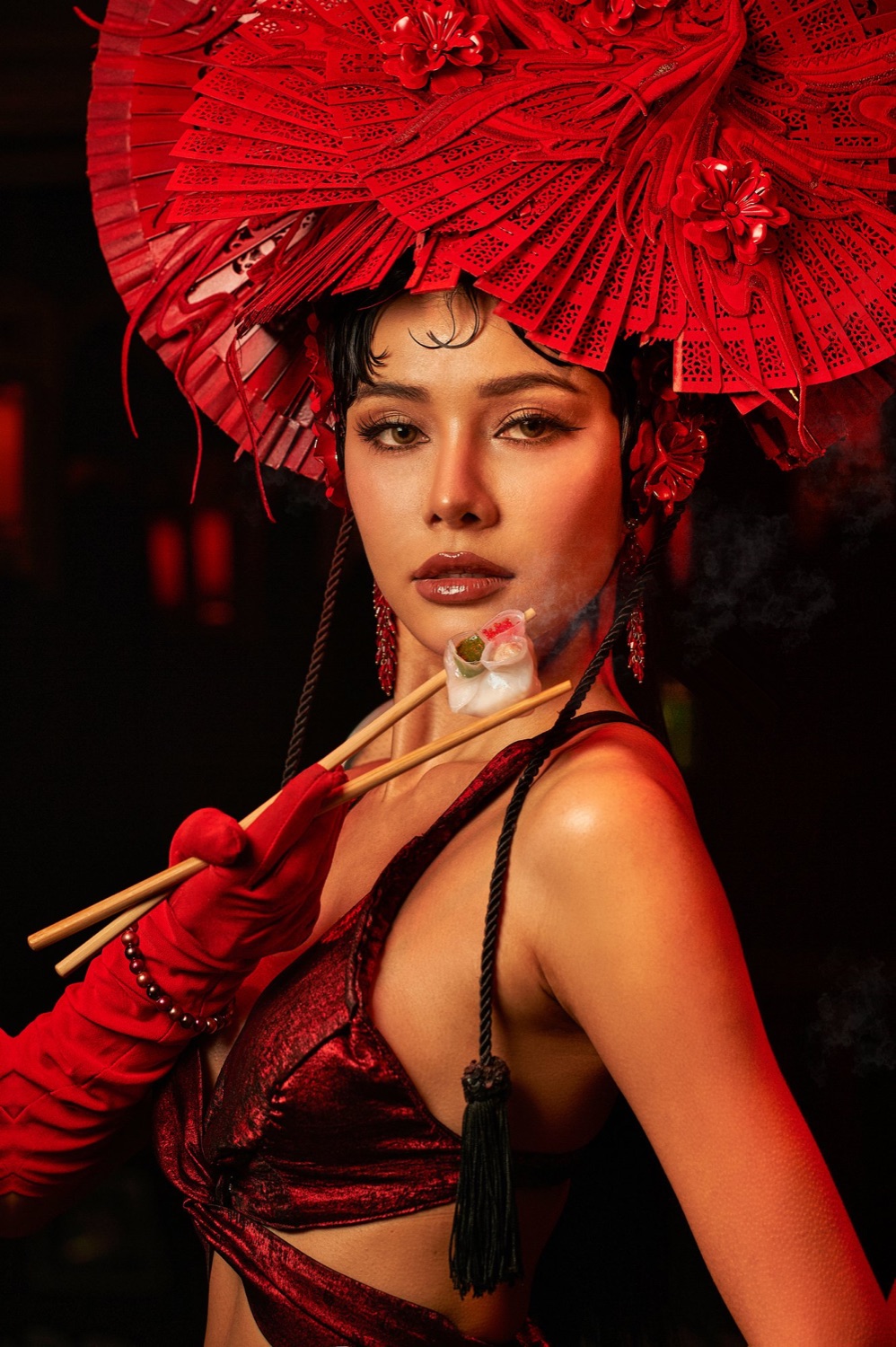 Performer in a red fan headdress holding a dumpling with chopsticks, Steam Room, Sing Sing Theater